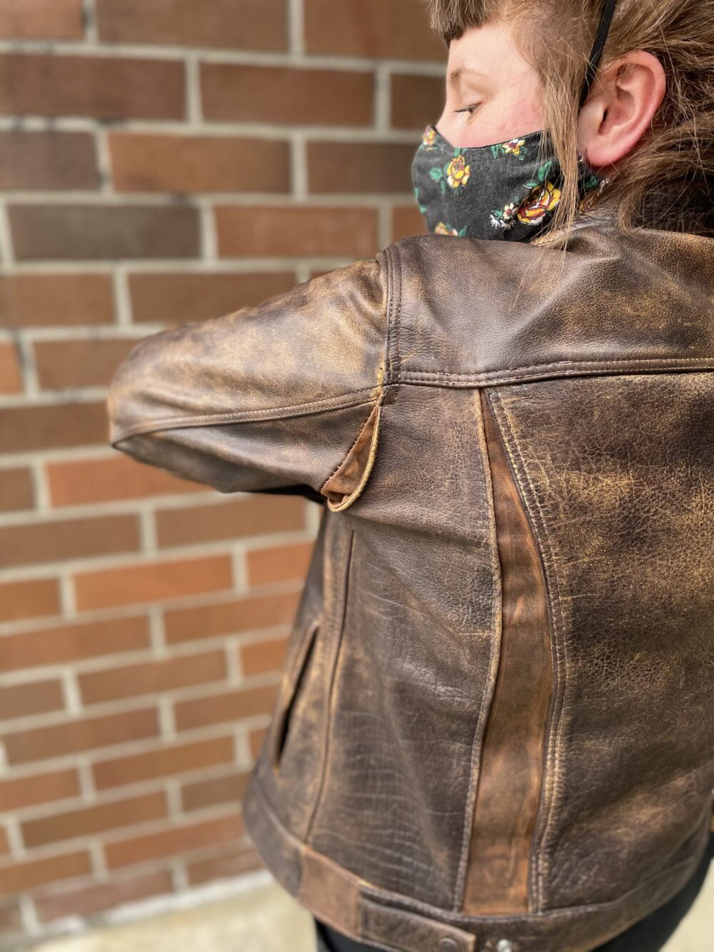 Tess bends arm to show small leather expansion panels added to the underarm and back of a brown leather jacket to make the jacket larger through the underarm, shoulders, and back.