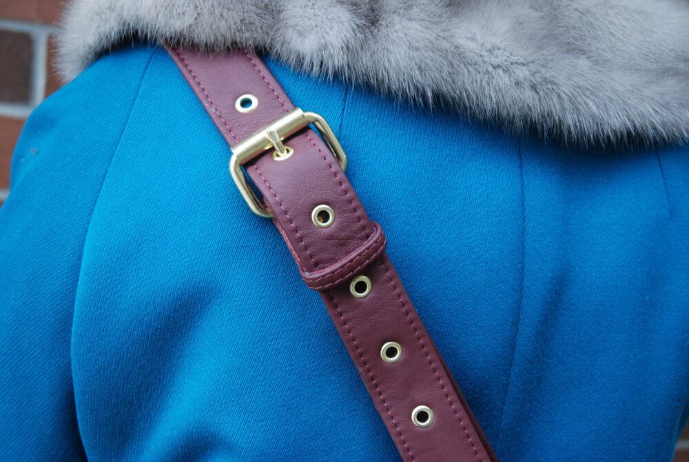 New burgundy leather strap with brass hardware, against blue jacket