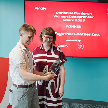 Tess and Ariss standing in front of a red background accepting the Christine Bergeron Award
