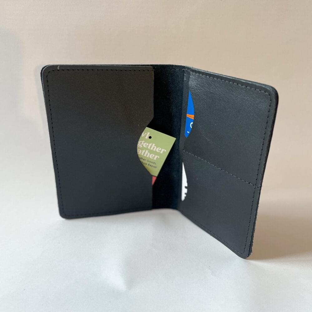 A black leather passport wallet with rounded corners standing open to show a full length slot on the left side of the wallet and a full length slot with 2 card slots overtop on the right.