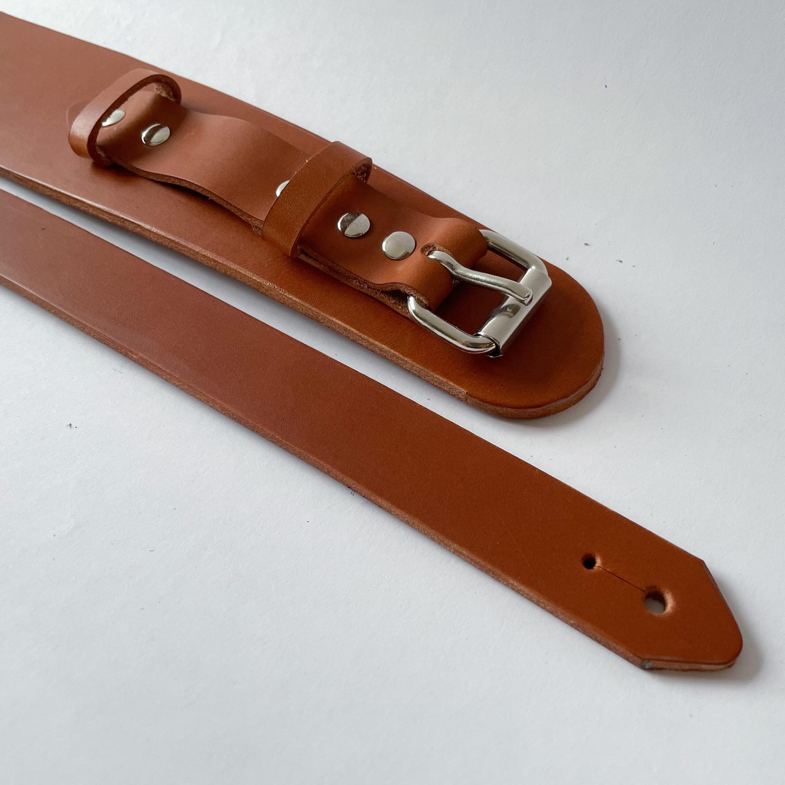 The ends of a flat light brown latigo leather guitar strap showing how they attach to a guitar with a hole for the peg hardware on one side and a strap to wrap around the neck.