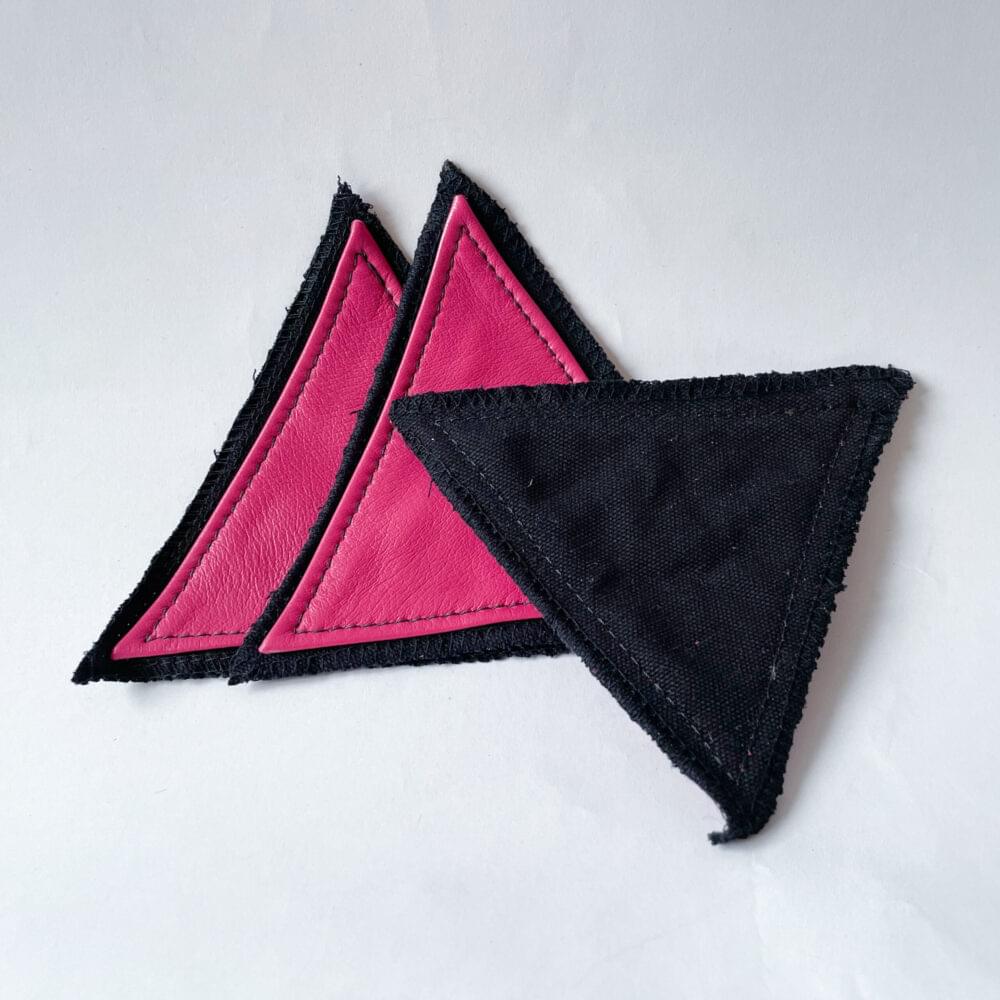 3 patches of pink leather triangles stitched onto a black fabric base, 2 with the right side, the pink side facing out and one flipped around to show just the black backing.